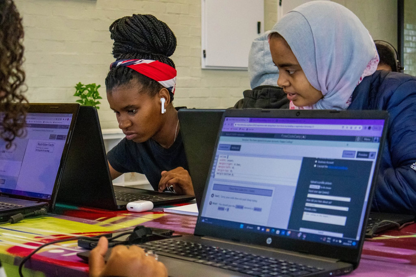 Learners coding on laptops side by side at a colourful table